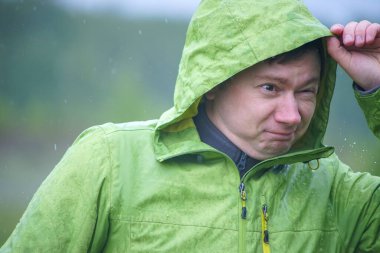 Yağmurluklu genç bir adam yağmurda duruyor. Yüzüne ve ceketine yağmur damlaları düşer..