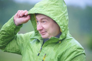 Yağmurluklu genç bir adam yağmurda duruyor. Yüzüne ve ceketine yağmur damlaları düşer..