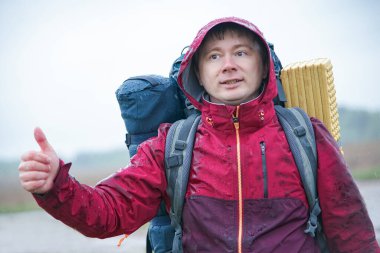 Sırt çantalı bir gezgin yolun kenarında durur ve yağmurda bir araba yakalar.