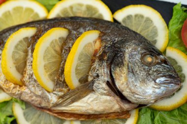 Fırında pişirilmiş Dorado balığı ve limon siyah bir taş tahtada yatıyor.