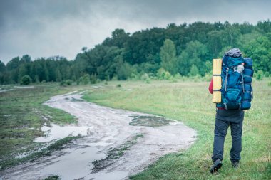 Turist yürüyüşçüsü yağmurda kırmızı ceketli bir sırt çantasıyla yolda yürüyor.