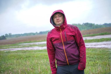 Yağmurlu bir gökyüzünün altında kırmızı kapüşonlu bir adam duruyor.