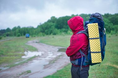 Turist yürüyüşçüsü yağmurda kırmızı ceketli bir sırt çantasıyla yolda yürüyor.