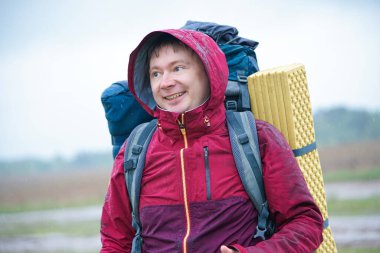 Turist çantalı bir yürüyüşçü dağlarda yağmurda gülümsüyor.