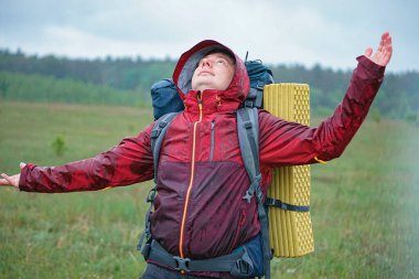 Turist çantalı bir yürüyüşçü dağlarda yağmurda gülümsüyor.