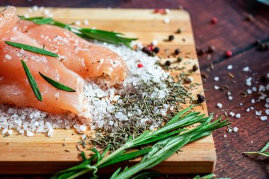 Kurutulmuş tavuk, üzerinde baharat ve deniz tuzu olan bir tahtada yatıyor. Biberiye, kakule, biber..