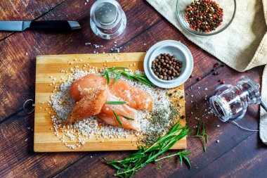 Kurutulmuş tavuk, üzerinde baharat ve deniz tuzu olan bir tahtada yatıyor. Biberiye, kakule, biber..