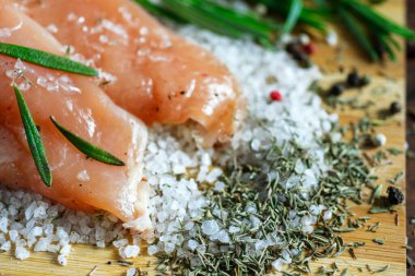 Kurutulmuş tavuk, üzerinde baharat ve deniz tuzu olan bir tahtada yatıyor. Biberiye, kakule, biber..
