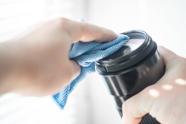 DSR kamerasının lenslerini temizlemek için bir mikrofiber bez tutan el lens camındaki tozu siler.