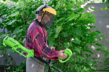 Bir adam evinin yanında elektrikli çim biçme makinesiyle çim biçiyor.