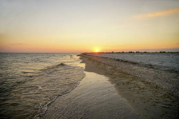 Deniz kenarında turuncu güneşli gün batımı. Dalga kıyıya vuruyor.