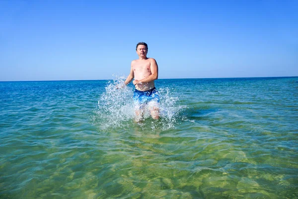 Adam denizdeki dalgalar boyunca masmavi suyla koşuyor. Sıçramalar yanlardan uçar.