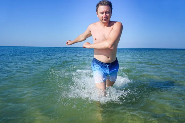 Adam denizdeki dalgalar boyunca masmavi suyla koşuyor. Sıçramalar yanlardan uçar.