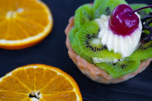 Yanında kivili ve kremalı pasta, portakal dilimleri var. Siyah arkaplan