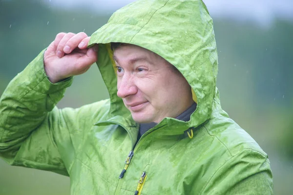 Yağmurluklu genç bir adam yağmurda duruyor. Yüzüne ve ceketine yağmur damlaları düşer..