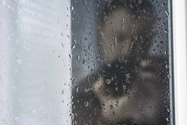 The photographer stands near the window with drops on the glass. The style displays a blurry reflection