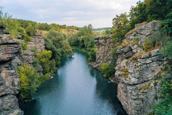 arge stone rocks with a river between them with clear water. Trees grow on the rocks.