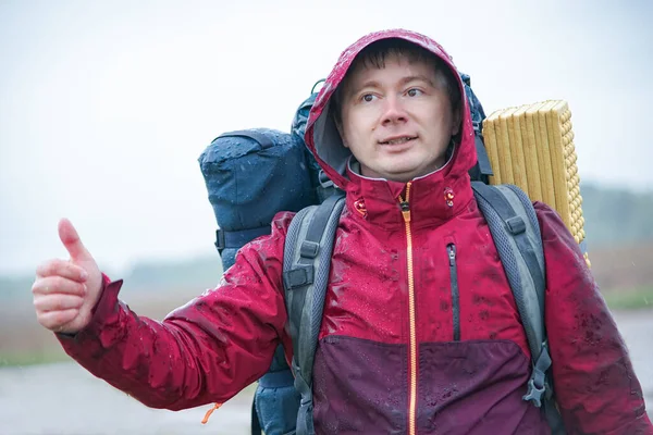 Sırt çantalı bir gezgin yolun kenarında durur ve yağmurda bir araba yakalar.