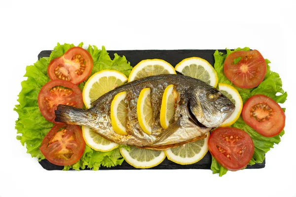 Fırında pişirilmiş Dorado balığı ve limon siyah bir taş tahtada yatıyor.