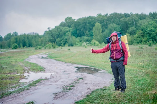 Turist yürüyüşçüsü kırmızı bir sırt çantasıyla yolda yürüyor.