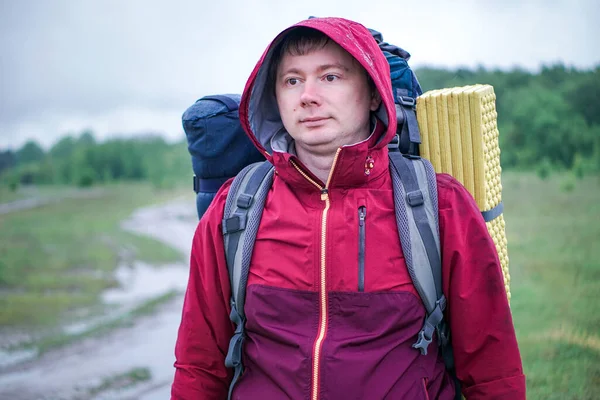 Turist yürüyüşçüsü yağmurda kırmızı ceketli bir sırt çantasıyla yolda yürüyor.