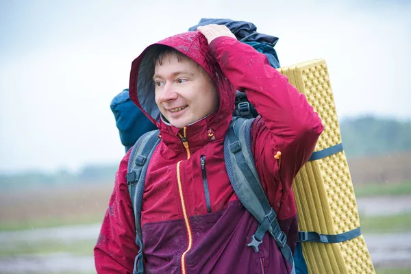 Turist çantalı bir yürüyüşçü dağlarda yağmurda gülümsüyor.