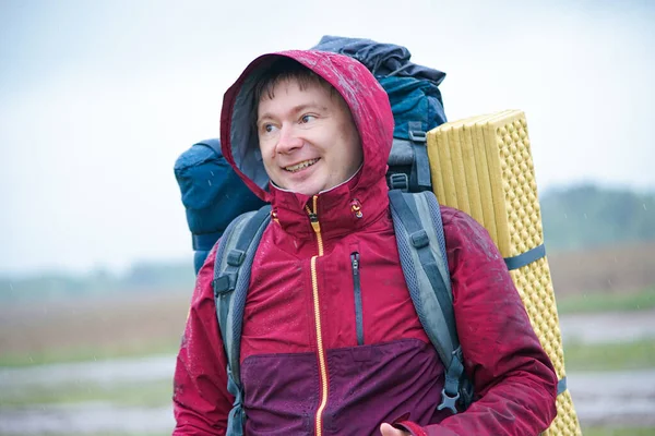 Turist çantalı bir yürüyüşçü dağlarda yağmurda gülümsüyor.