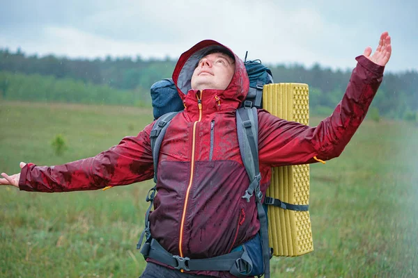 Turist çantalı bir yürüyüşçü dağlarda yağmurda gülümsüyor.