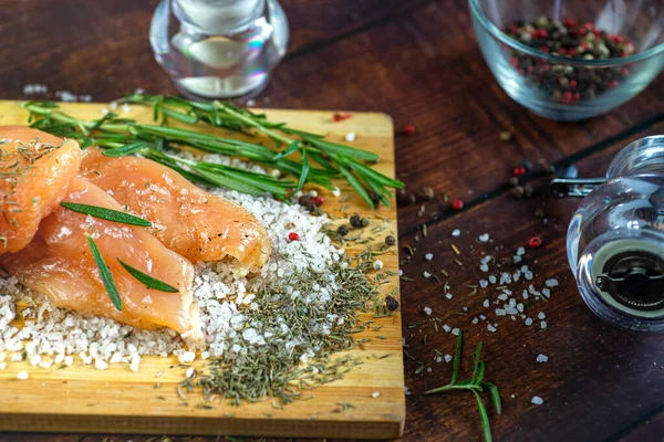 Kurutulmuş tavuk, üzerinde baharat ve deniz tuzu olan bir tahtada yatıyor. Biberiye, kakule, biber..