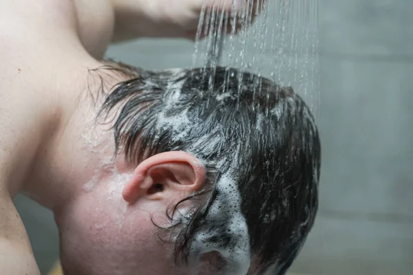 Banyodaki adam saçını duşta şampuanla yıkıyor.