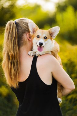 Arkaya bakan kız omuzunda galsh corgi tutuyor.