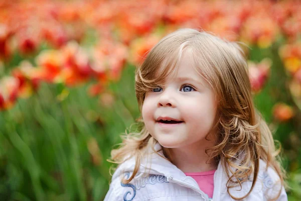 Милая кудрявая блондинка, улыбающаяся с удивлением на тюльпане. — стоковое фото