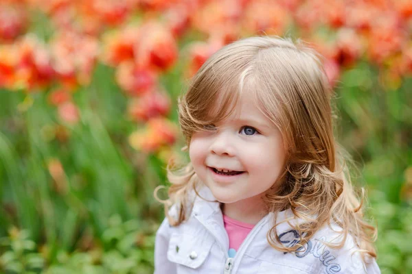 Süße lockige Haare blondes Mädchen lächelt mit Überraschung auf Tulpenbloss — Stockfoto