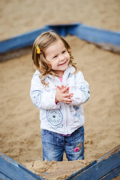 Милая маленькая девочка играет с песком на детской площадке — стоковое фото