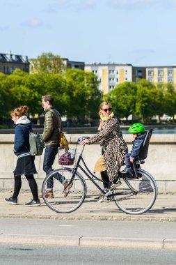 Copenhagen, Danimarka - 03 Mayıs 2018: Genç kadın binicilik bisiklet güvenlik miğfer onun arkasında da çocuk Bisiklet arka koltukta oturan bir çocukla. Sokak tarzı. Güvenli ve çocuk koruma kavramı