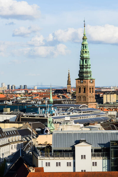 Aerial cityscape shot of old roofs, Nikolaj Kunsthal and Church of Our Saviour from the top of Rundetaarn Round Tower, famous Oresund Bridge between Sweden and Denmark on horizon, Copenhagen