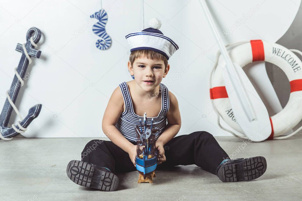 Cabin boy in sailor cap playing with model of ship