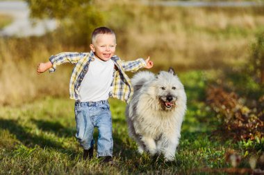 Mutlu gülümseyen sarışın çocuk çiftlikte köpek arkadaşıyla koşuyor.