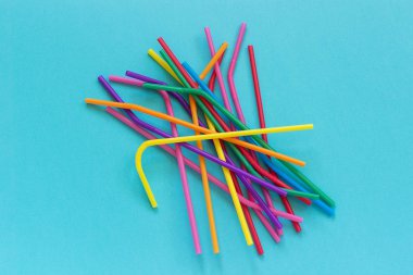Mavi arka plan üzerinde kokteyller ve içecekler için plastik tek kullanımlık çok renkli içme pipetleri yığını. Üstte Görüntüle Kopyalama alanı