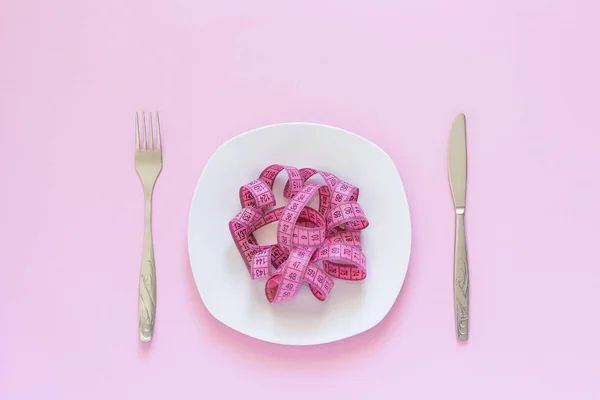 Cinta métrica rosa acostada en placa en forma de espagueti, cuchillo y tenedor sobre fondo rosa — Foto de Stock