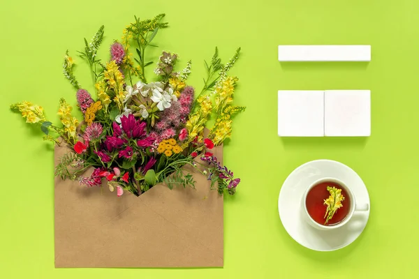 Empty wooden cubes calendar Mock up tamplate for your calendar date Cup of herbs tea kraft envelope with colorful flowers on green background. Concept hello spring or summer Creative Top view Flat lay — Stock Photo, Image