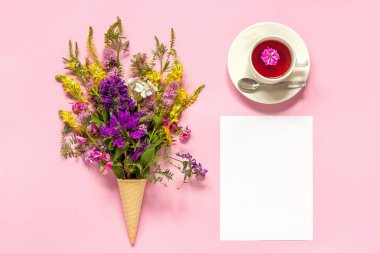 Buket renkli kır çiçekleri dondurma waffle koni, çay fincan ve pembe arka plan Creative Top view Flat Lay Mock şablonu kartpostal veya tasarım için metin için boş boş kağıt kart