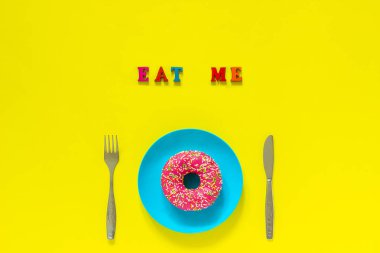 Mavi plaka ve sarı arka plan üzerinde çatal bıçak çatal beni Pembe donut yiyin.