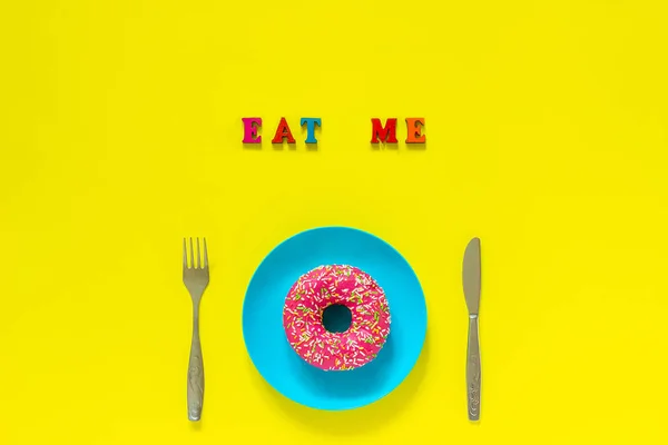 Cómeme rosado donut en plato azul y cuchillo tenedor sobre fondo amarillo . — Foto de Stock