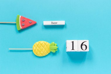 Tahta küplerin takvimi 16 Haziran ve yaz meyveleri ananas şekeri, mavi arka planda karpuz lolipopları. Tatil veya tatil kavramlarını kabul et Yaratıcı Üst Görünüm Düz Şablonu