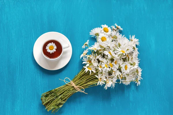 Bouquet Flowers field Chamomiles Cup of Herbal Tea on blue woode