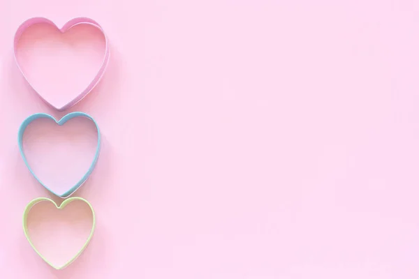 Coloridas galletas de corte en forma de corazón sobre fondo rosa pastel. Concepto tarjeta de San Valentín. Vista superior Copiar espacio para texto — Foto de Stock
