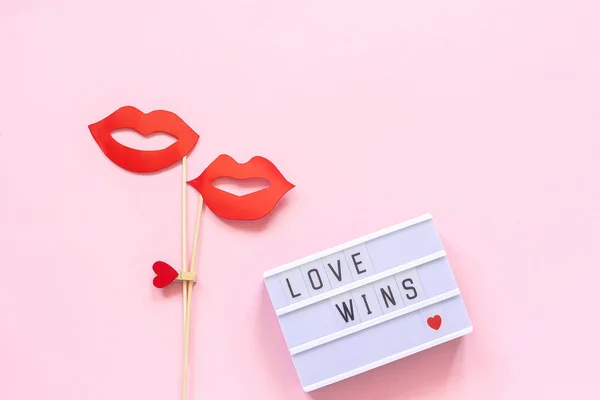 Lightbox with text Love wins and couple paper lips props on stick on pink background. Concept lesbian love National Day Against Homophobia Creative Valentine\'s Day Greeting card Top view