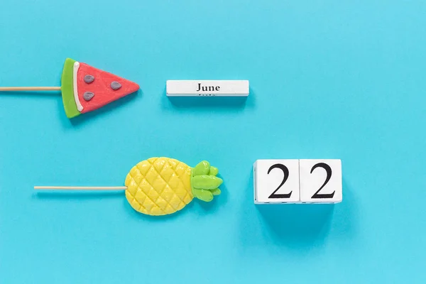 Wooden cubes calendar date June 22nd and summer fruits candy pineapple, watermelon lollipops on stick on blue background. Concept vacation or holidays Creative Top view Flat lay Template — ストック写真