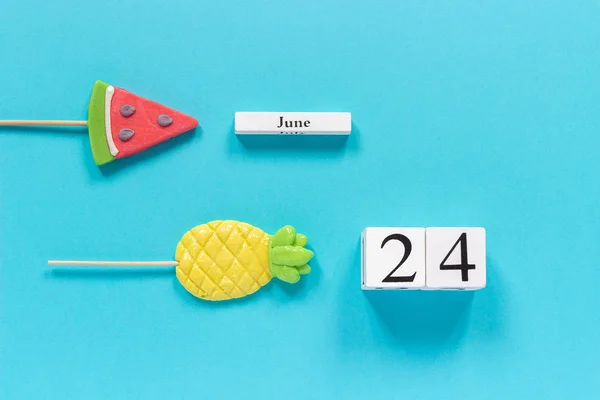 Dřevěné kostky kalendář datum 24. června a letní ovoce sladké ananas, vodní meloun lízátka na tyčinky na modrém pozadí. Koncept dovolená nebo dovolená Creative Top View Flat lay Template — Stock fotografie